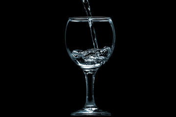 Pour water into glass on black background.