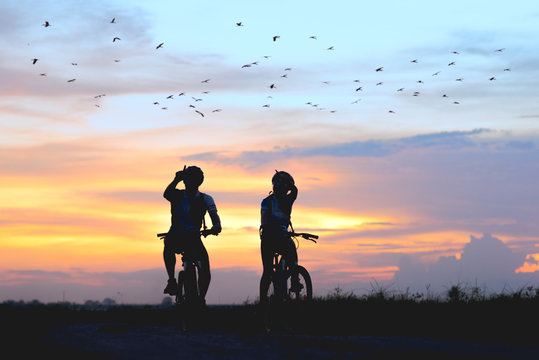 silhouette of couple lover biker cyclist riding enjoyment to the field of meadow lake at sunset, adventure bicycle wild and journey activity
