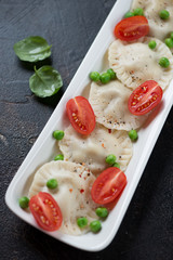Close-up of vareniki or dumplings with green peas and cherry tomatoes, vertical shot
