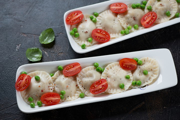 Two plates with ravioli, cherry tomatoes and green peas, studio shot over dark brown stone background