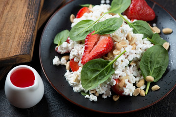 Closeup of salad with cottage cheese, spinach leaves, strawberries and nuts, studio shot