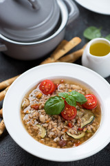 Italian spelt and minestrone soup topped with cherry tomatoes and fresh green basil, vertical shot