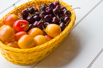  sweet cherries and ripe apricots in a yellow basket on a white wooden background