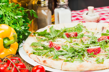 Homemade italian pizza, fresh cherry tomatoes and basil, arugula served on wooden board