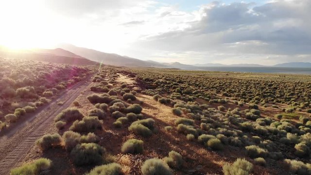 Flying Over Dirt Road in Nevada Desert with Sun Flare.