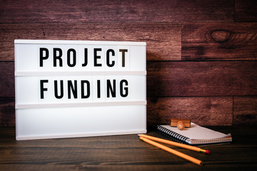 Project Funding. Text in lightbox. Wooden office table