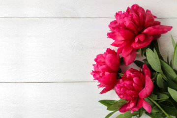 Frame of beautiful bright pink peony flowers on a white wooden background. top view. space for text
