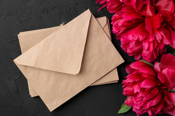 Beautiful bright pink flowers peonies and a stack of envelopes on a black graphite background. top view.