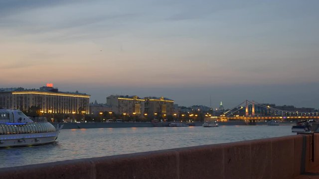 tourists ship sails on river against lit buildings in dusk