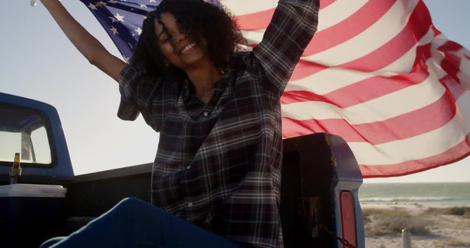 Mixed-race woman sitting with waving American flag on a pick up truck.
