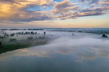 Forest lake in the morning fog, in the rays of the dawn sun. Drone view.