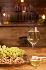 Glass of white wine with fresh grapes and wolnuts on a wooden plate in a vintage restaurant