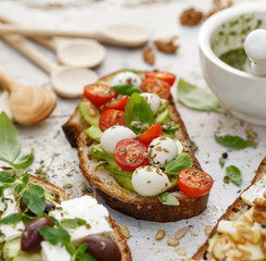 Open sandwiches, in the middle of board an open avocado sandwich made of slice of sourdough bread with the addition of cherry tomatoes, mini mozzarella, fresh basil, olive oil and oregano, close-up