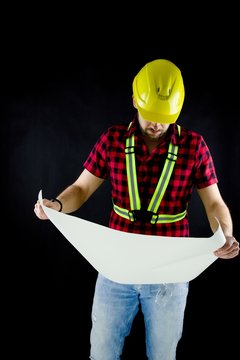 Construction Worker  on black background views the building plan.Construction worker with yellow crash helmet. Builder  on black baground.  He views the building plan.