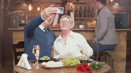 Romantic old couple taking a selfie during while they are having lunch in a restaurant