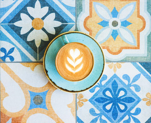 Coffee with latte art in blue cup on colorful tile background.