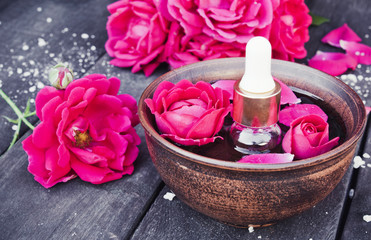 Bowl with red rose petals on a background of dark wooden boards and essential oil with roses.