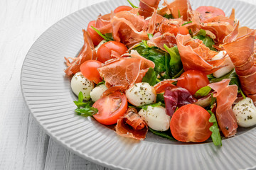 Salad with fresh vegetables with dried tomatoes, meat and mustard, mozzarella, prosciutto