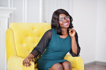 Obraz premium Pretty african american woman in eyeglasses posed in room sitting on yellow chair.