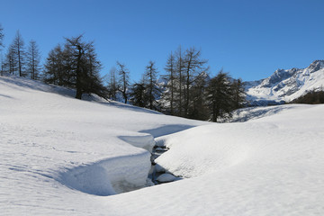 Italian Alps, Valle d'Aosta, Italy. A small stream flow in the middle of the snow.