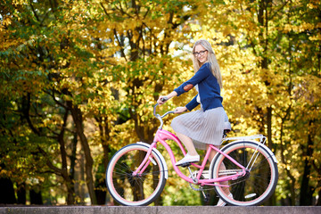 Side view of active blond long-haired attractive woman in glasses, skirt and blouse riding modern...