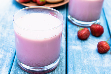Cocktail with milk and berries club in a glass against the background of blue boards.