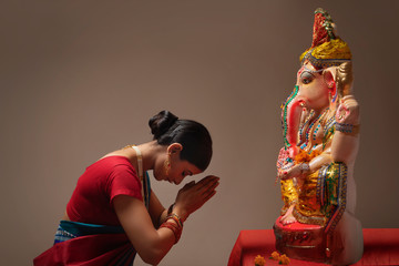 Woman praying with hands joined and eyes closed in front of Ganpati Idol.