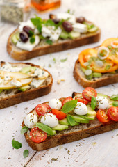 Assorted open faced sandwiches, Open avocado sandwiches made of slices of sourdough bread with various toppings  on a white wooden table, top view. Delicious and nutritious breakfast