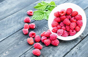 Fresh raspberry with leaves on the background of old dark boards. Selective focus.
