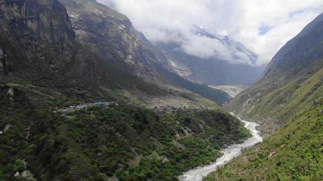 Aerial ascent showing a small Himalayan village in Nepal with large beautiful mountains, clouds and fog in the background. Seq 1