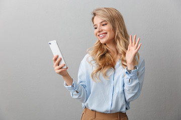 Naklejka premium Photo of caucasian blond businesswoman with long curly hair smiling and waving at smartphone in hand