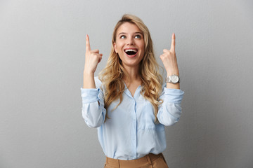 Photo of happy blond businesswoman with long curly hair smiling and pointing fingers upward at...