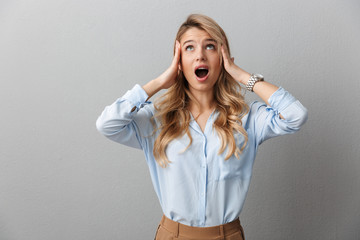 Photo of displeased blond businesswoman with long curly hair screaming and grabbing her head