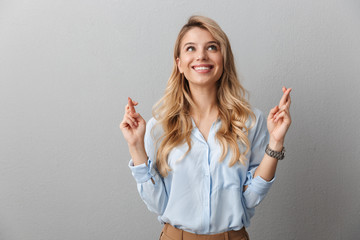 Photo of elegant blond businesswoman with long curly hair smiling and keeping fingers crossed wishing good luck