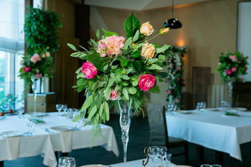 Beautiful flower arrangement in a vase on a high stem for a party, wedding reception or other festive event. Glassware and cutlery for catered event dinner