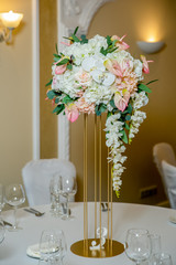 Beautiful table setting with crockery and white flower arrangements in a vase on a high stem for a party, wedding reception or other festive event. Glassware and cutlery for catered event dinner