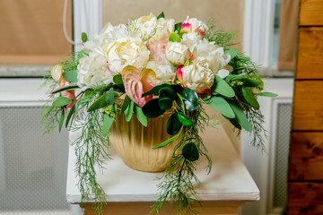 A white bouquet of peonies, hortensia and anthurium in a gold flowerpot on a white pillar in a classic style