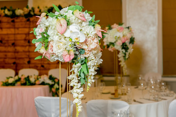 Beautiful table setting with crockery and white flower arrangements in a vase on a high stem for a party, wedding reception or other festive event. Glassware and cutlery for catered event dinner