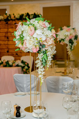 Beautiful table setting with crockery and white flower arrangements in a vase on a high stem for a party, wedding reception or other festive event. Glassware and cutlery for catered event dinner