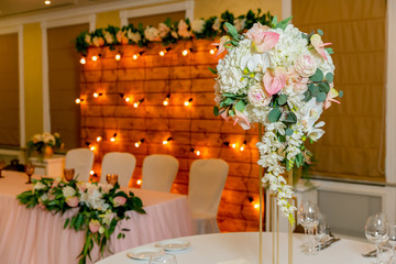Beautiful table setting with crockery and white flower arrangements in a vase on a high stem for a party, wedding reception or other festive event. Glassware and cutlery for catered event dinner