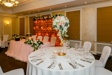 Beautiful table setting with crockery and white flower arrangements in a vase on a high stem for a party, wedding reception or other festive event. Glassware and cutlery for catered event dinner