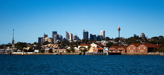 City Harbourside houses, wharf and boat sheds on Sydney Harbour with city CBD skyline in background...