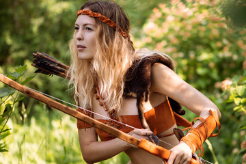 Beautiful girl archer with long blond hair with a bow and arrows dressed in leather