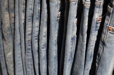 Jeans trousers hanging on a shop rack, a side view, a closeup. Denim textile background, blurry (shallow depth of field).