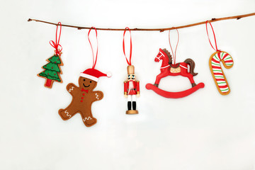 Christmas decorations hanging on a branch with nutcracker soldier, tree, candy cane and gingerbread man on white background with copy space.