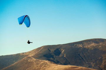 Paraglider flying over mountains in sunny day. Freedom concept. Soaring flight moment. Paragliding...