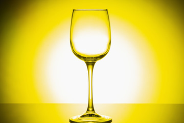 Wine glass on a gleam on a white-yellow background. Close up.