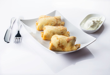 Pancakes with a meat, eggs and onions stuffing. Sour cream. White background. Close up. Selective focus.