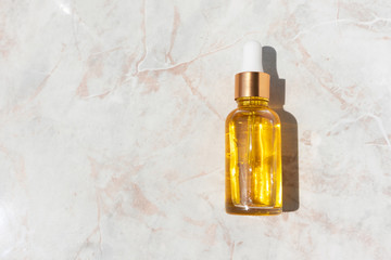Oily serum in glass bottle with pipette on marble background with copy space. Luxury cosmetic