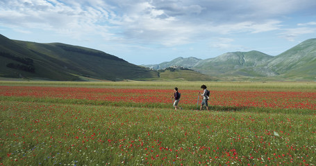 Aerial view flying above two people couple hiking or nordic walking outdoor on a trail path near flower fields in Castelluccio di Norcia.Approaching forward. Friends italian trip in Umbria.4k drone